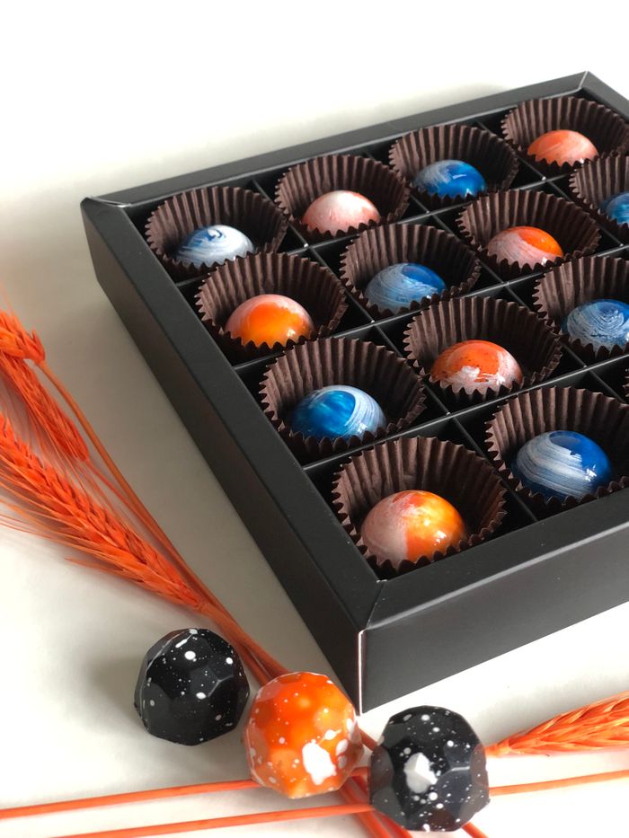 Home Elegant box of colorful marble-patterned chocolates with decorative orange grass on a neutral background.