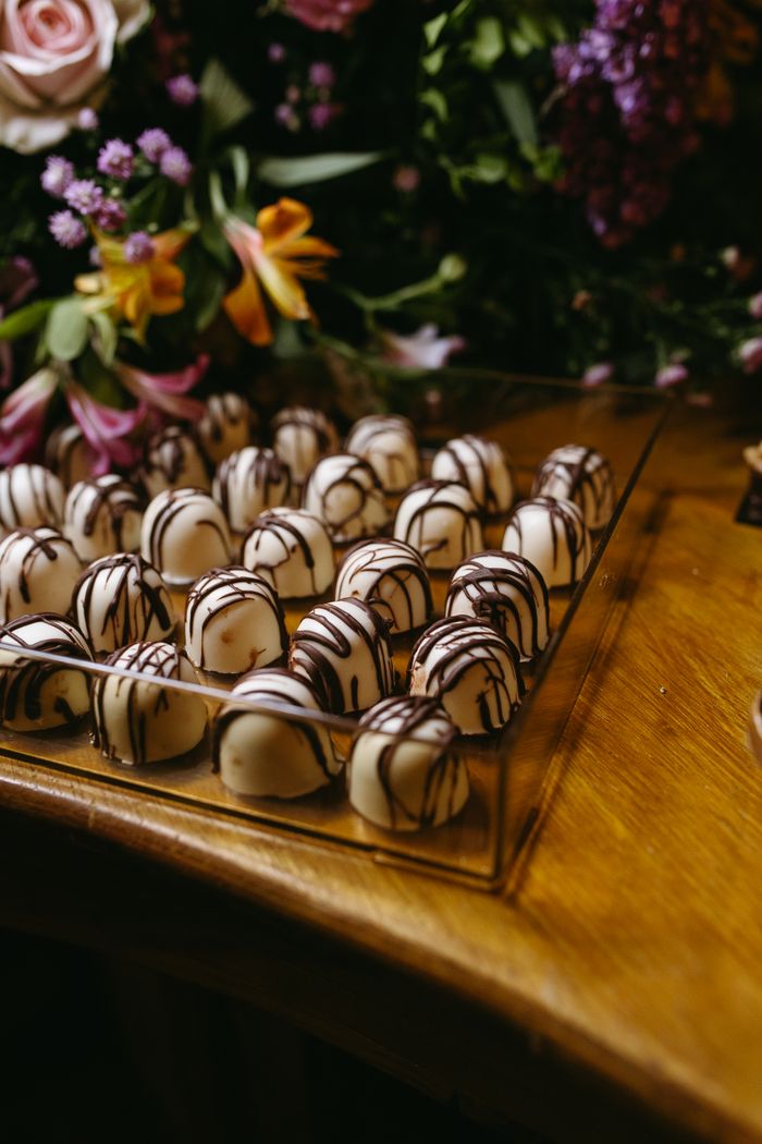 Home Gourmet chocolate truffles with drizzled design surrounded by a vibrant flower arrangement.