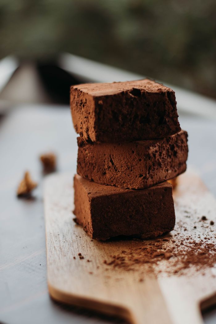 Home Three stacked chocolate brownies with cocoa powder on a wooden board. Perfect for dessert imagery.
